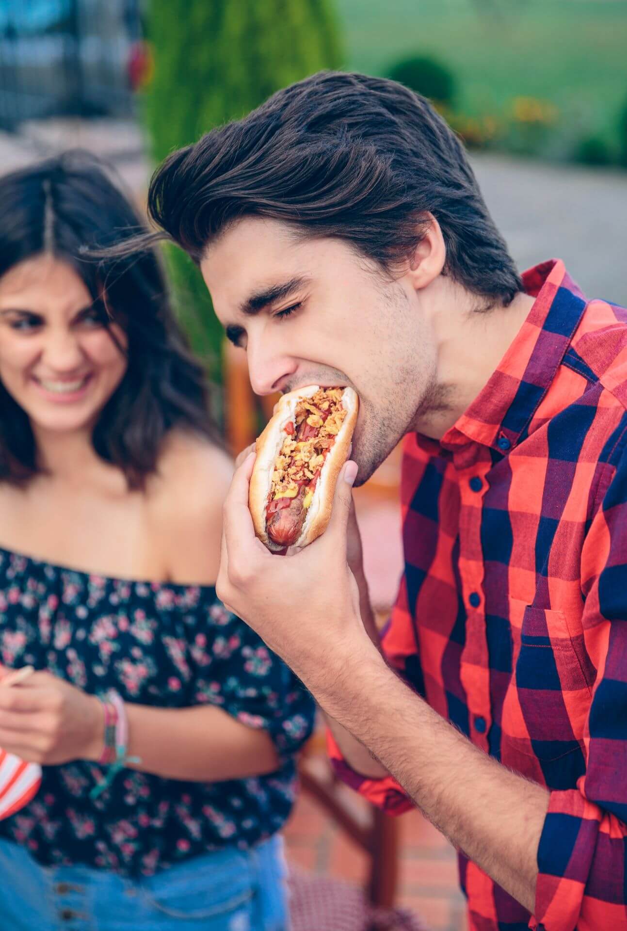 young-man-eating-hot-dog-and-woman-laughing-in-bac-2025-03-13-02-27-01-utc.jpg